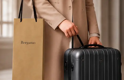 Bergamoの縦長ショッパーバッグを肘に掛け、スーツケースを持つ女性